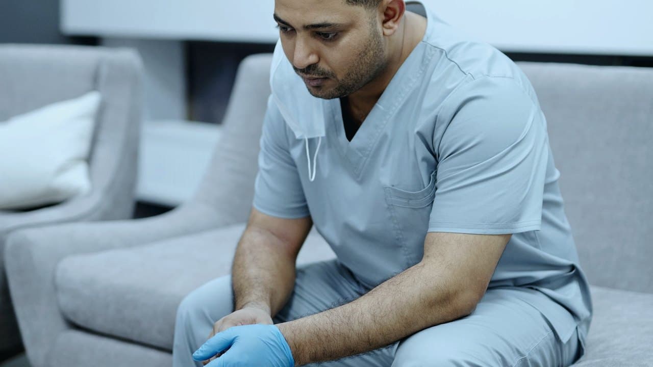 مراقب سلامت در اسکراب خسته نشسته روی مبل، نماد خستگی نوبت‌کاری