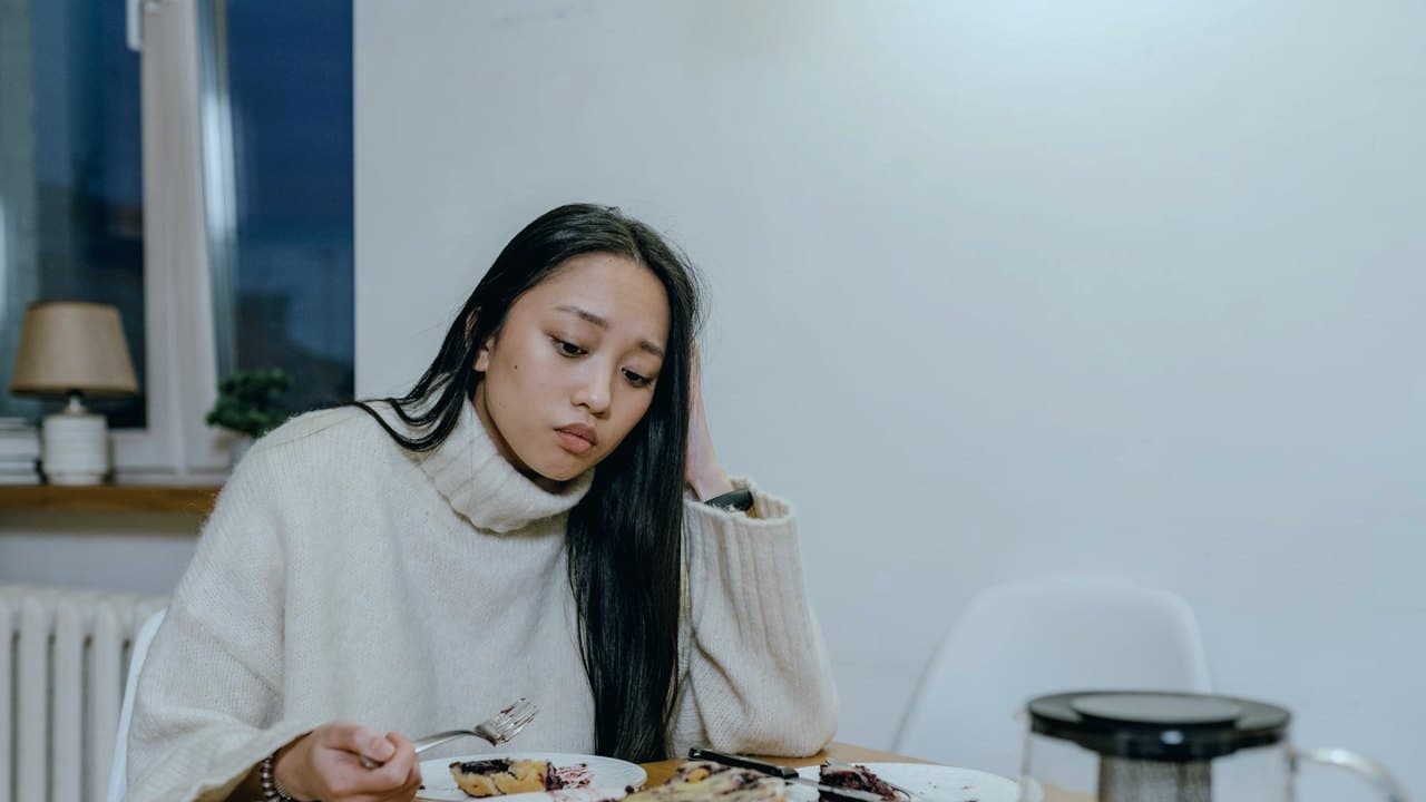 زن پشت میز غذا با نگاه دور از بشقاب، نماد اجتناب و بیعلاقگی به غذا